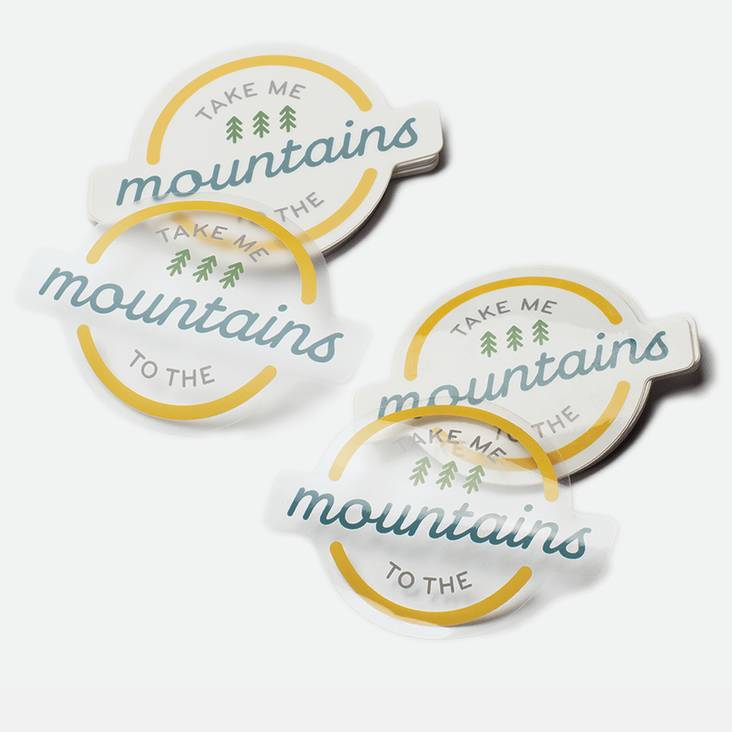 Two stacks of clear stickers one glossy and one matte printed by StickerGiant with take me to the mountains printed on them