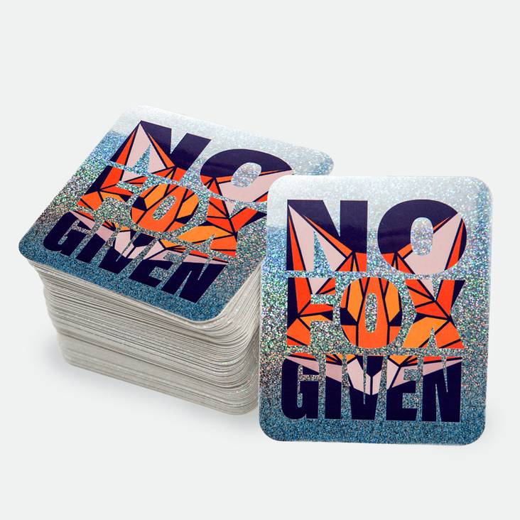 A No Fox Given Glitter Sticker printed by StickerGiant in front of a stack of glitter stickers
