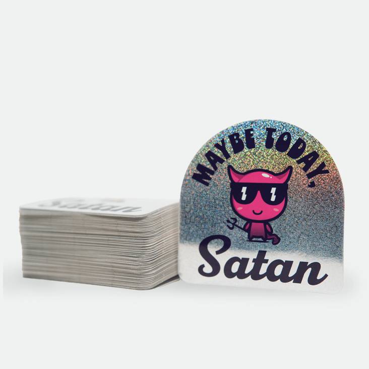 A Maybe Today Satan Glitter Sticker printed by StickerGiant next to a stack of stickers
