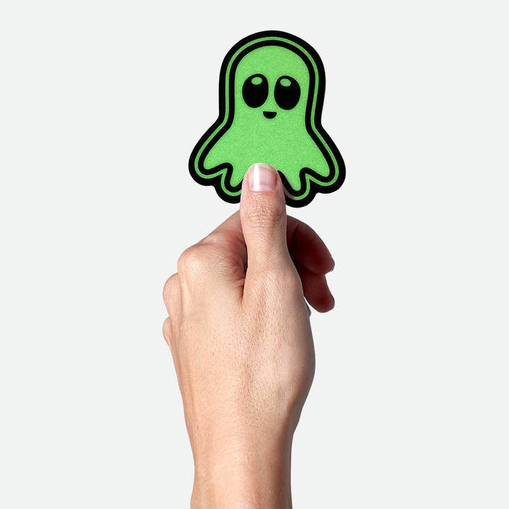 A hand holding a glow in the dark ghost shaped sticker printed by StickerGiant
