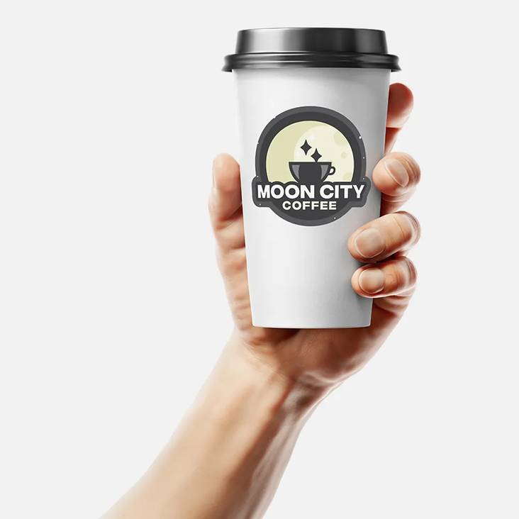 Hand holding a to go coffee cup with a Moon City Coffee die cut sticker printed by StickerGiant applied to the side