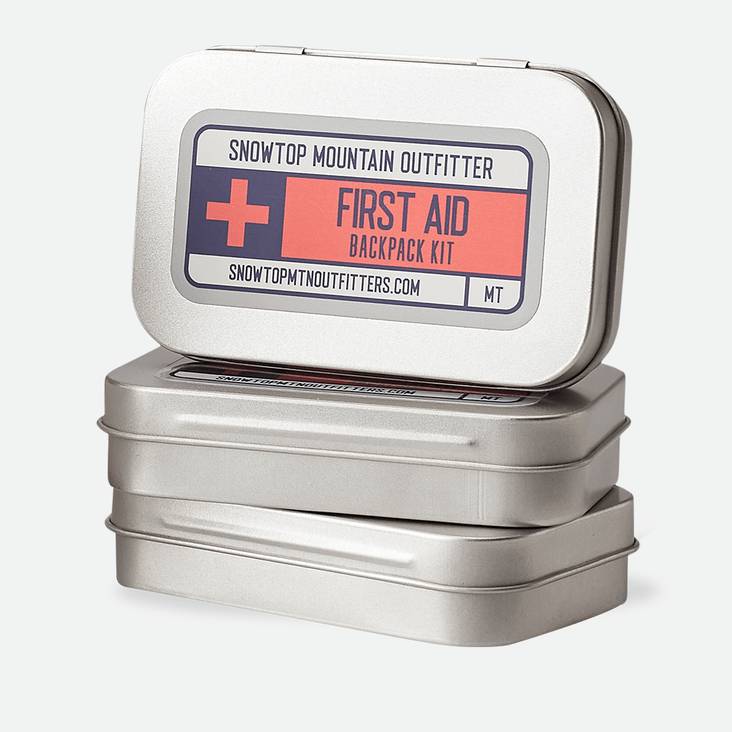 A stack of metal tins with Snowtop Mountain Outfitter First Aid Kit matte label printed by StickerGiant applied to the top of the tin